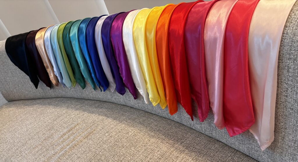 Colorful silk scarves arranged in a gradient on a sofa.